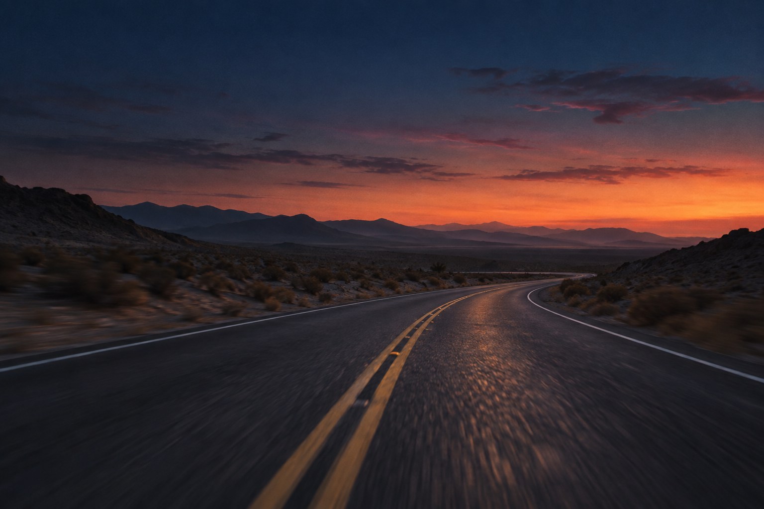 An empty winding road disappearing into a dusky blue horizon